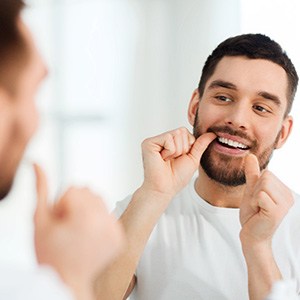Young man with a beard flossing in the mirror
