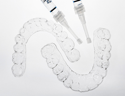 Custom teeth whitening trays and bleaching gel kit on a white surface 